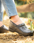 Black clogs with a flower pattern styled with light jeans.