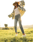 A woman in white clogs, jeans, a quilted shirt, and a wide-brim hat. 