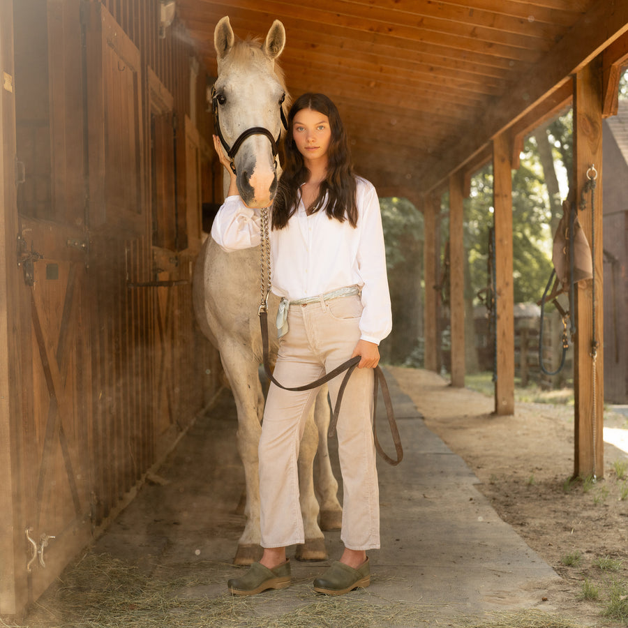 Girl standing with a horse in green suede clogs and stylish tan pants.