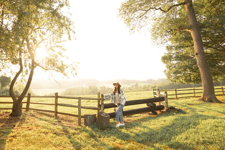 Woman in quilt jacket and jeans wearing stylish white clogs in an open field.