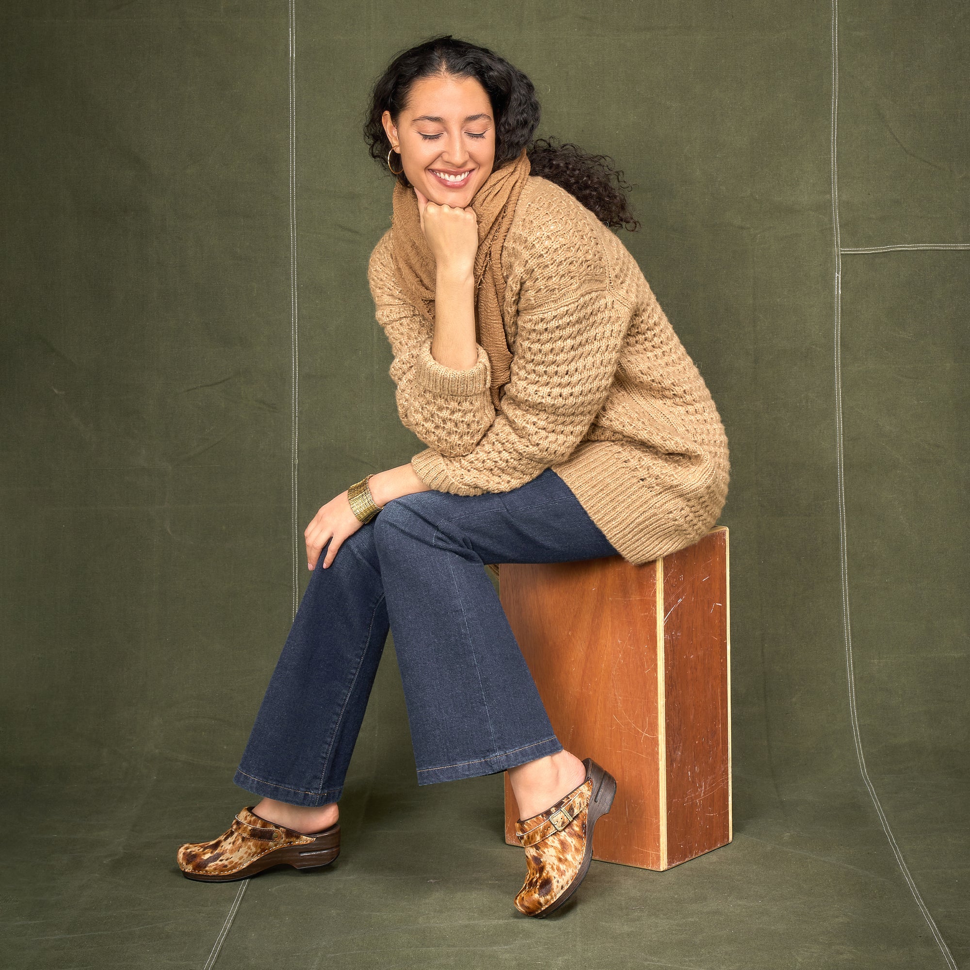 A woman smiling in a cozy sweater and spotted haircalf slingback clogs.