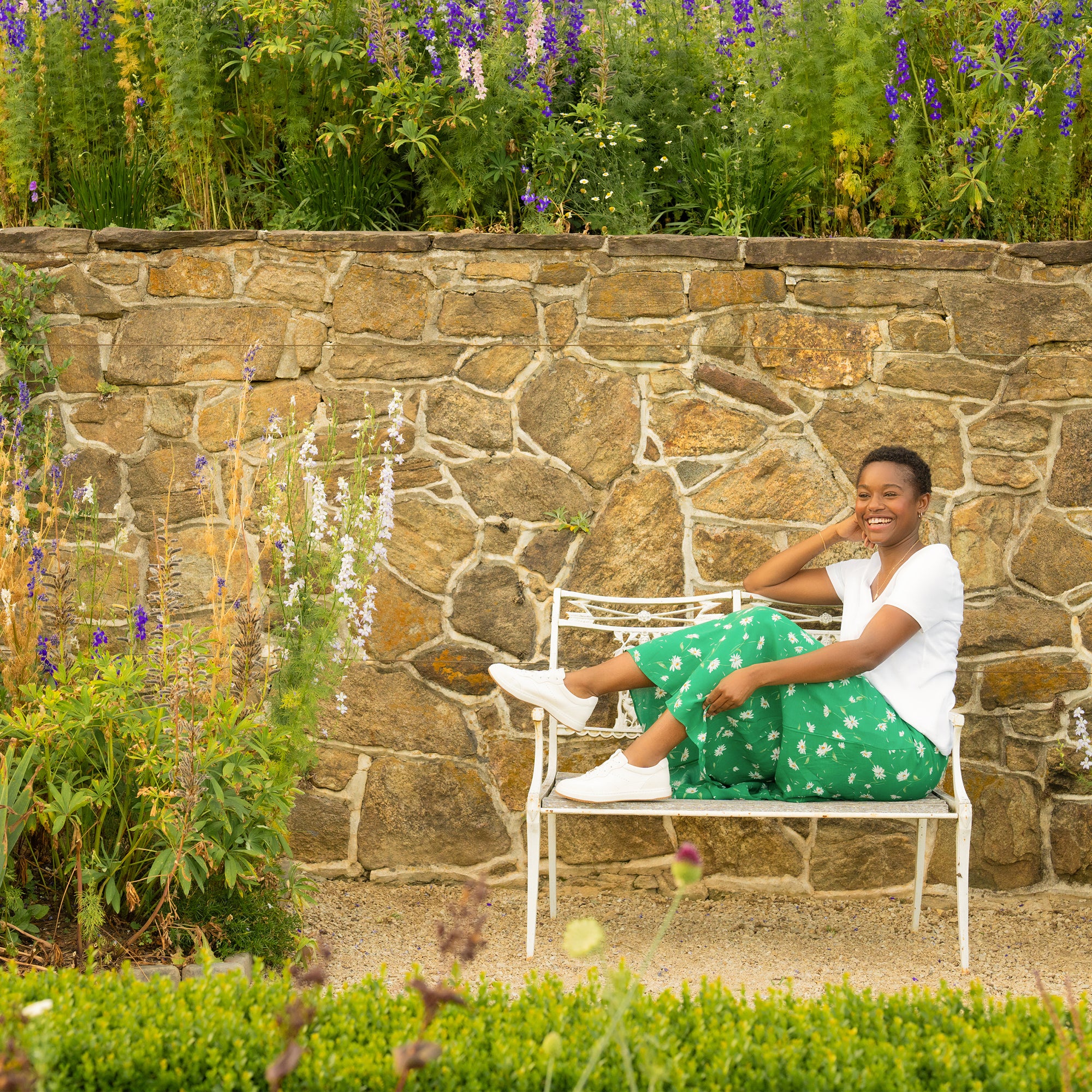 A woman on a bench in a casual skirt and t shirt wearing lightweight white leather sneakers.