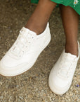 A pair of casual white leather sneakers shown on foot.