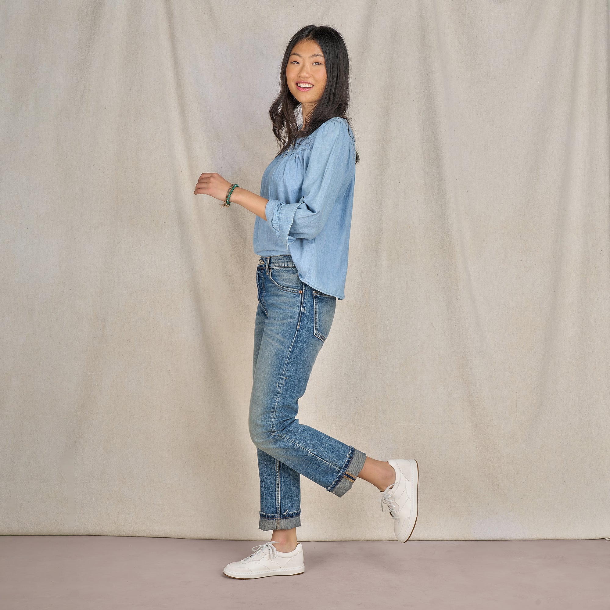 A woman in denim attire wearing casual white leather sneakers.