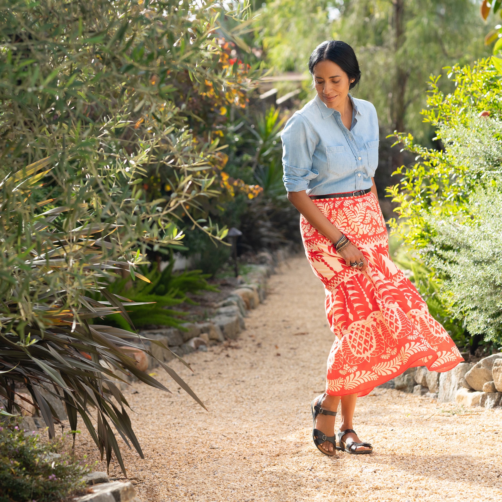 A woman in a bright skirt standing on a nature trail while wearing flat multi-strap sandals.