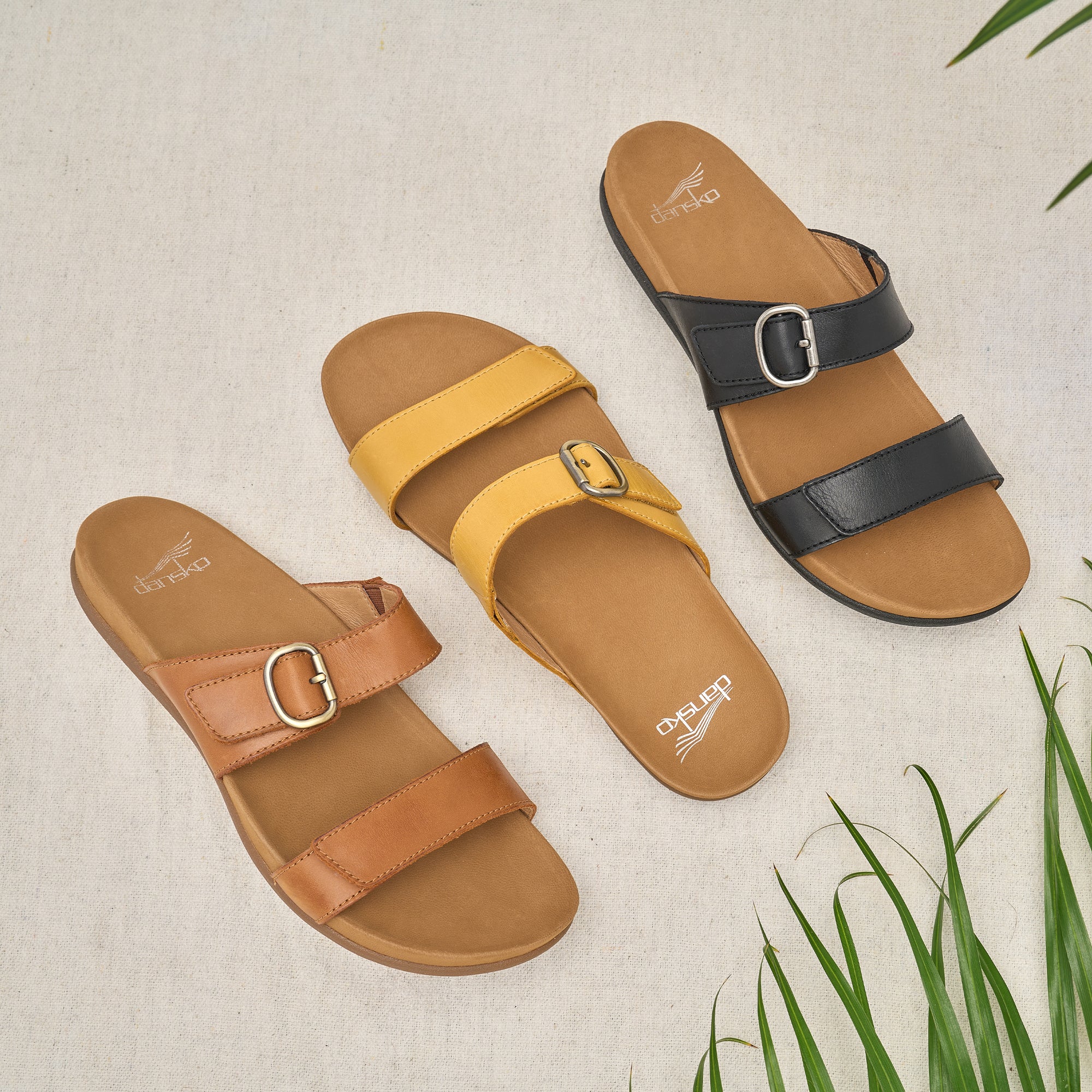 Three color options of a slide sandal with leather uppers and a contoured footbed.