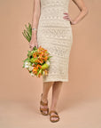 A woman in a dress holding flowers and wearing brown leather slide sandals.