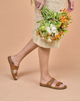 A woman in a dress holding flowers and wearing brown leather slide sandals.