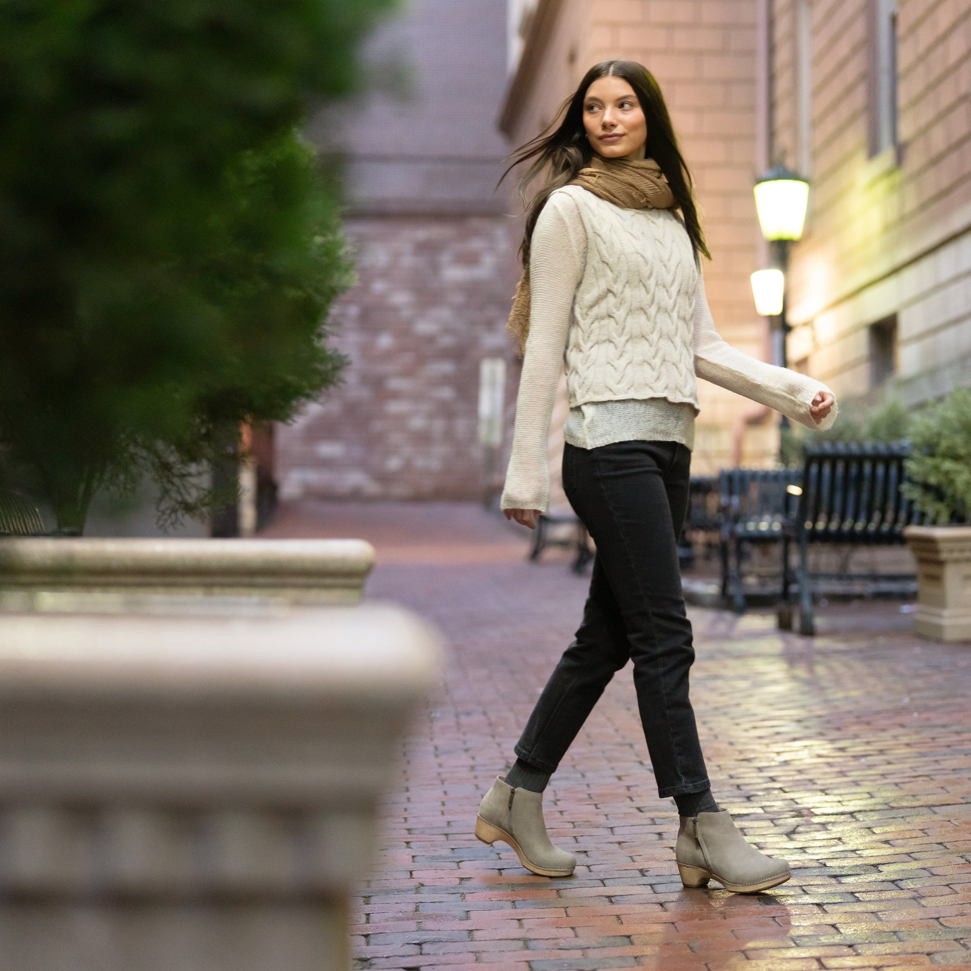 A woman in casual fall attire wearing gray leather booties with faux wooden soles.