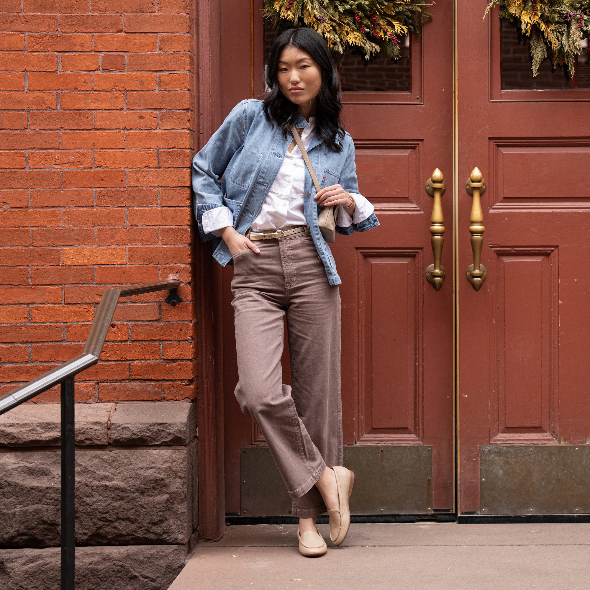 A woman standing in a doorway in a casual outfit wearing light tan flat loafers.