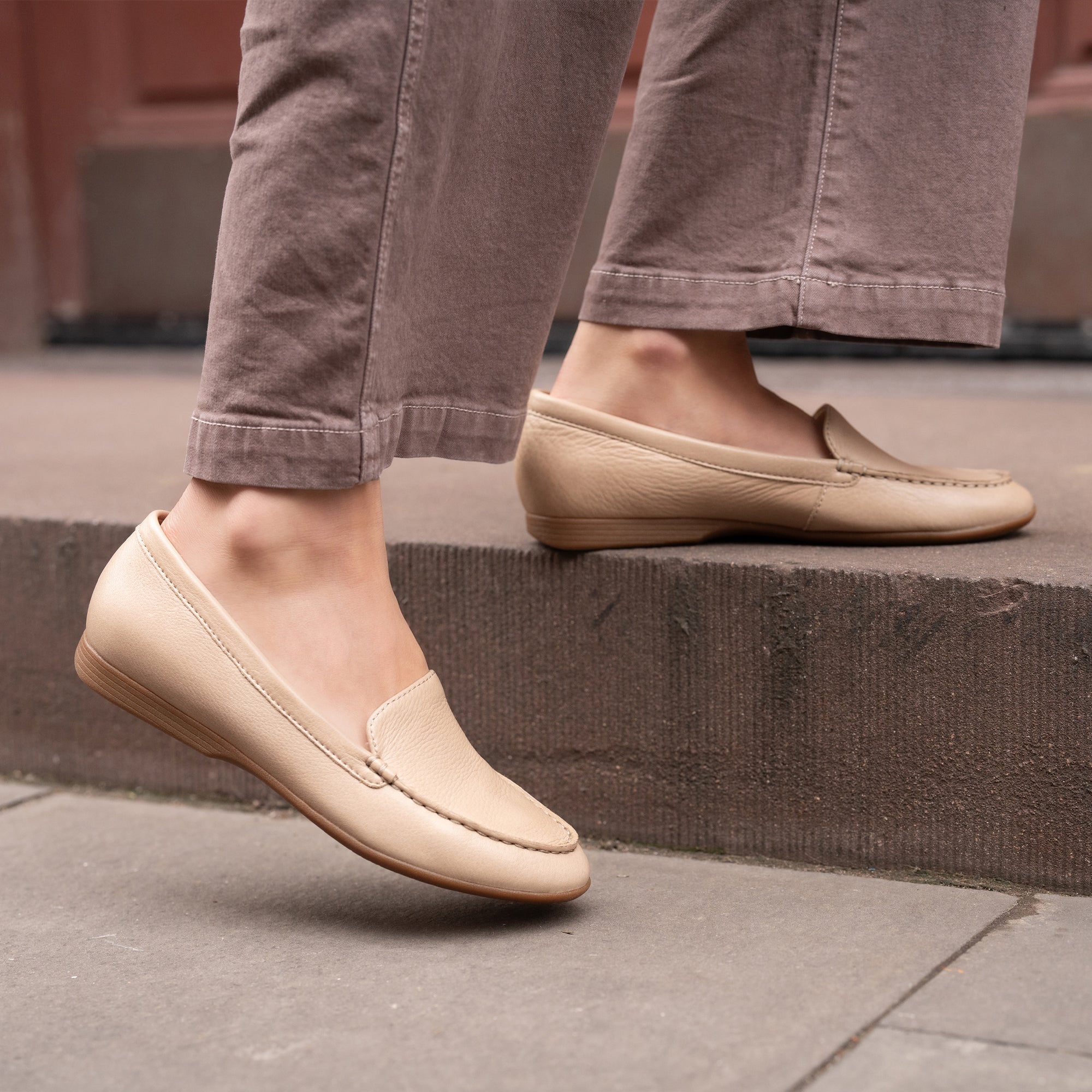 A closeup of tan flat loafers shown on foot.