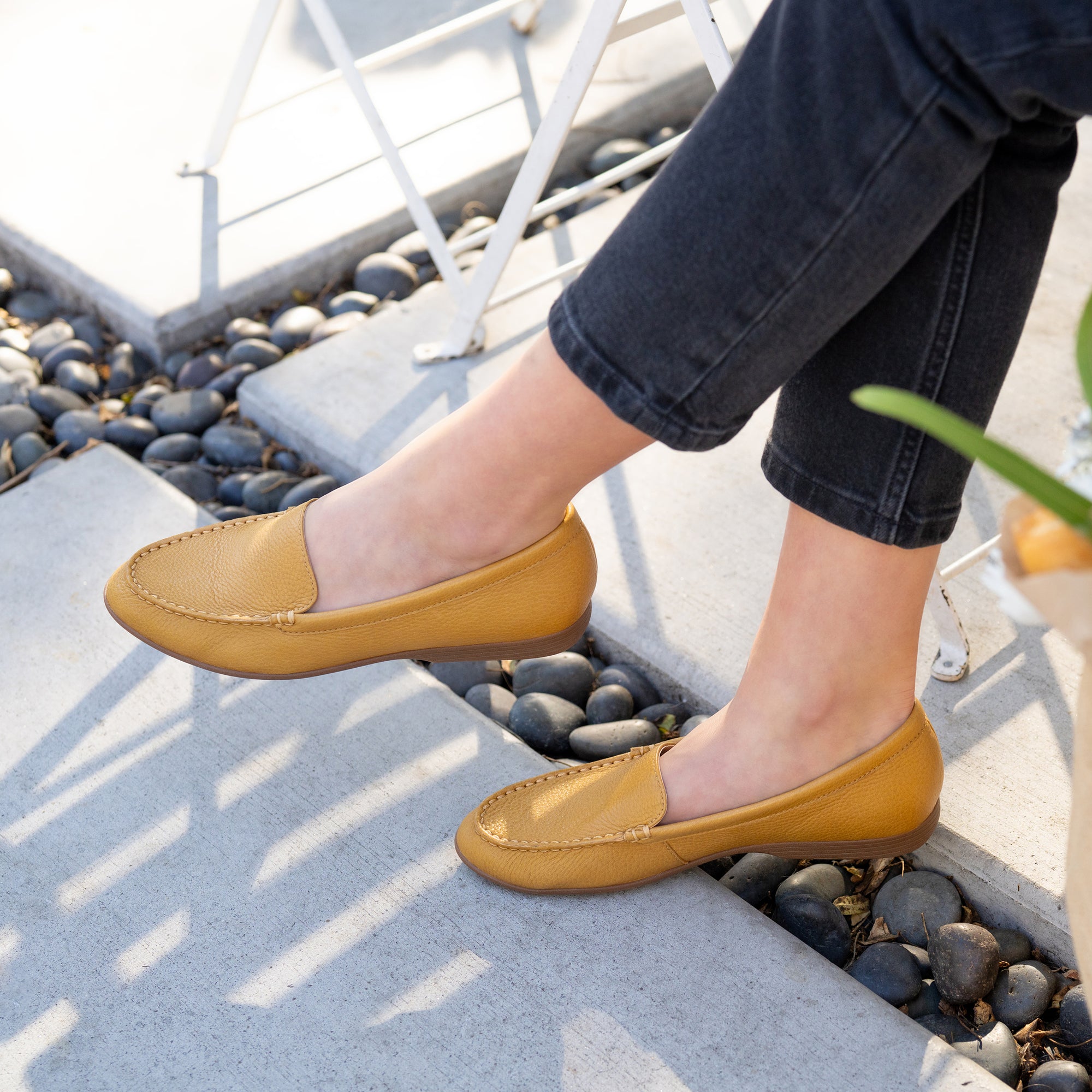 A closeup of mustard flat loafers shown on foot.