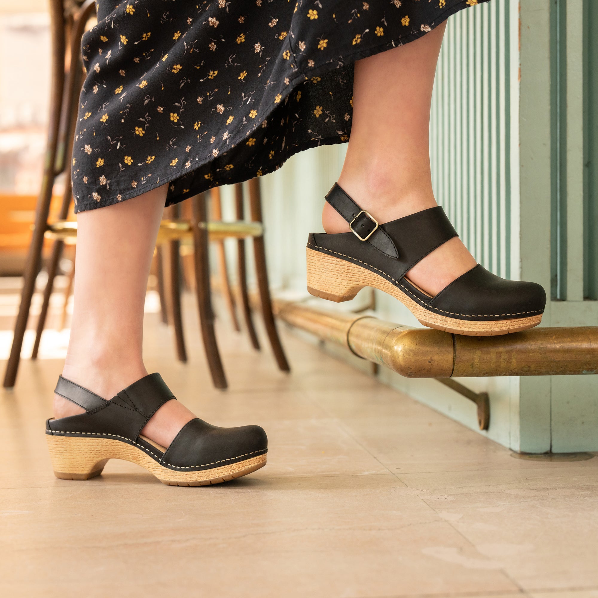 A closeup of black transitional sandals shown on foot.