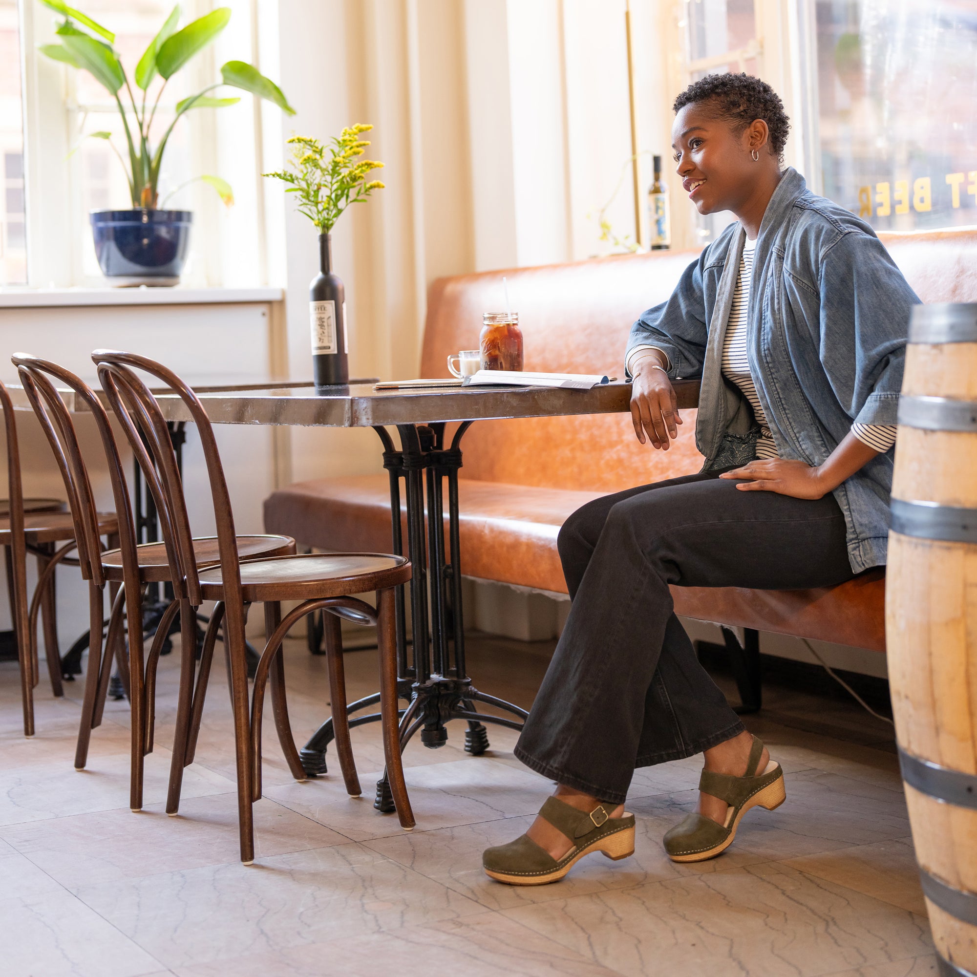 A woman sitting in a cafe in casual clothes wearing ivy transitional sandals.