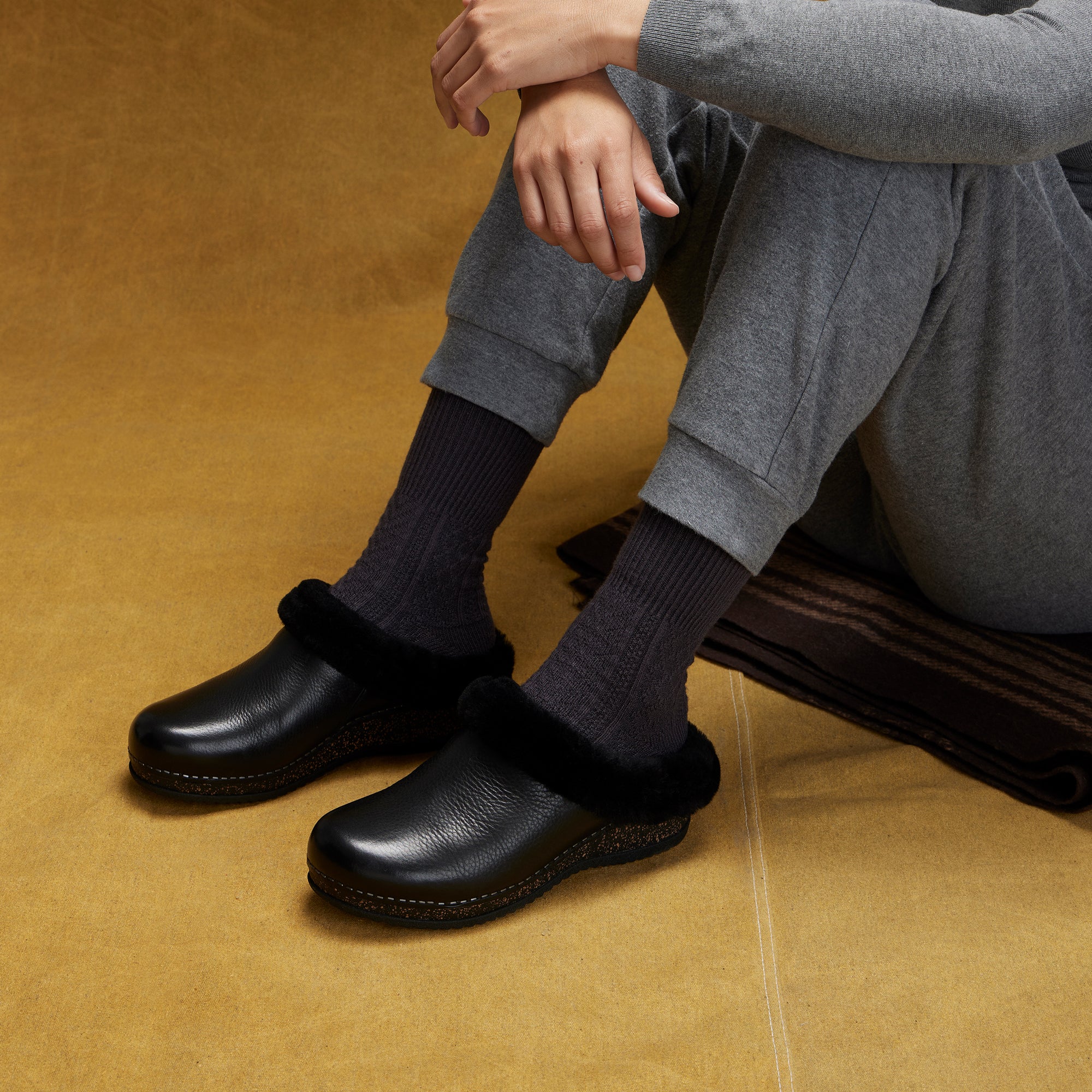 An on-foot look at black mule clogs with a black shearling cuff.