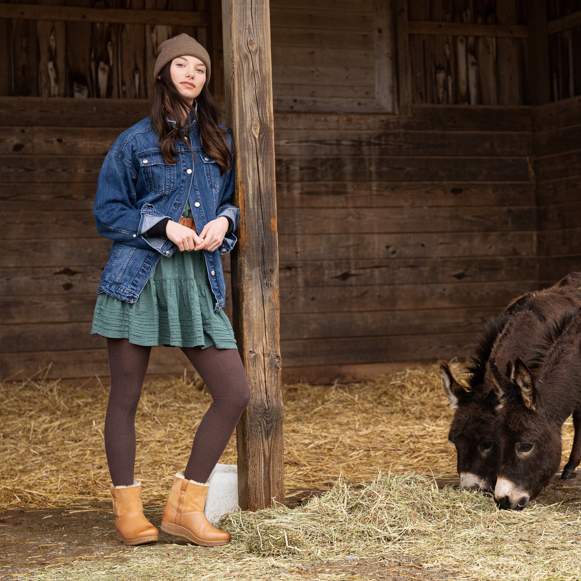 A woman earing faux-fur lined booties while standing with donkeys.