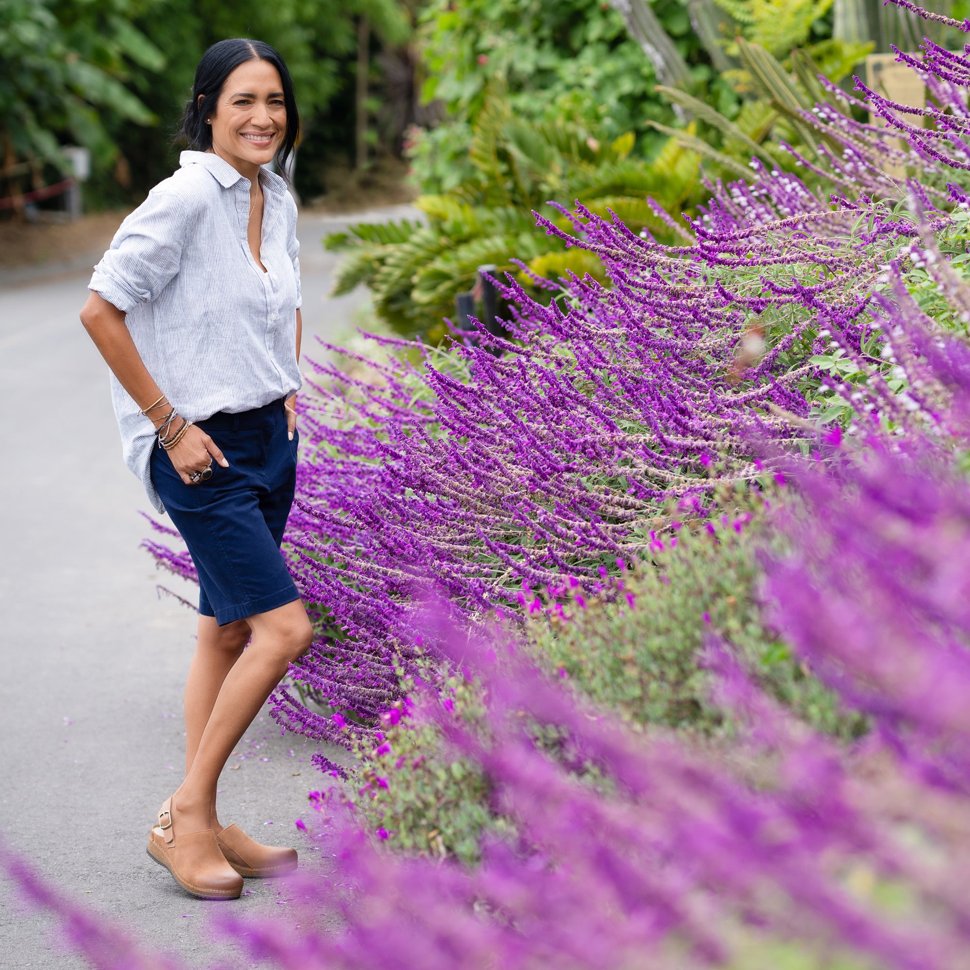 A woman standing amongst lavender flowers wearing tan clogs with a heel strap.