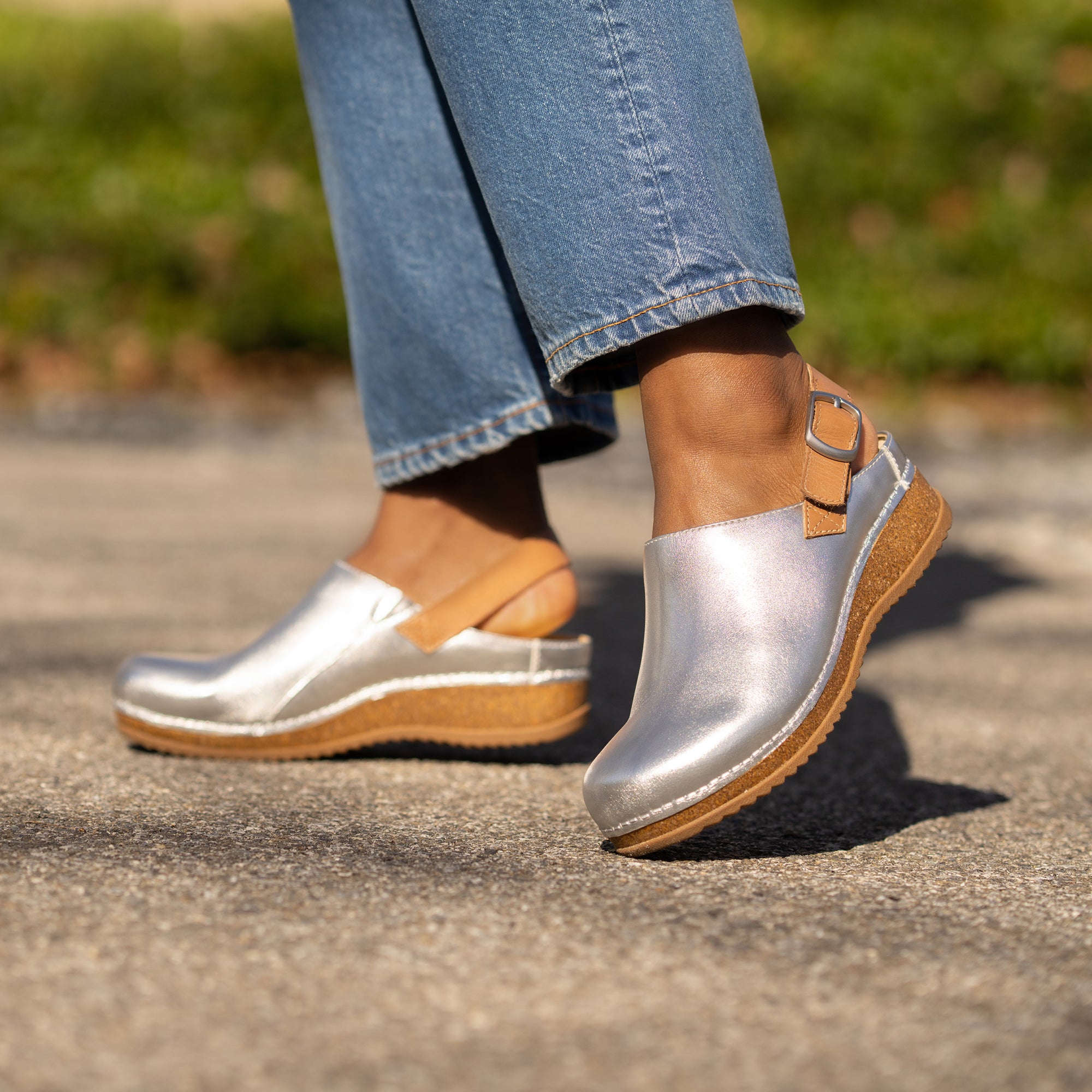 Silver metallic leather clogs with a heel strap and cork-based soles shown on foot.