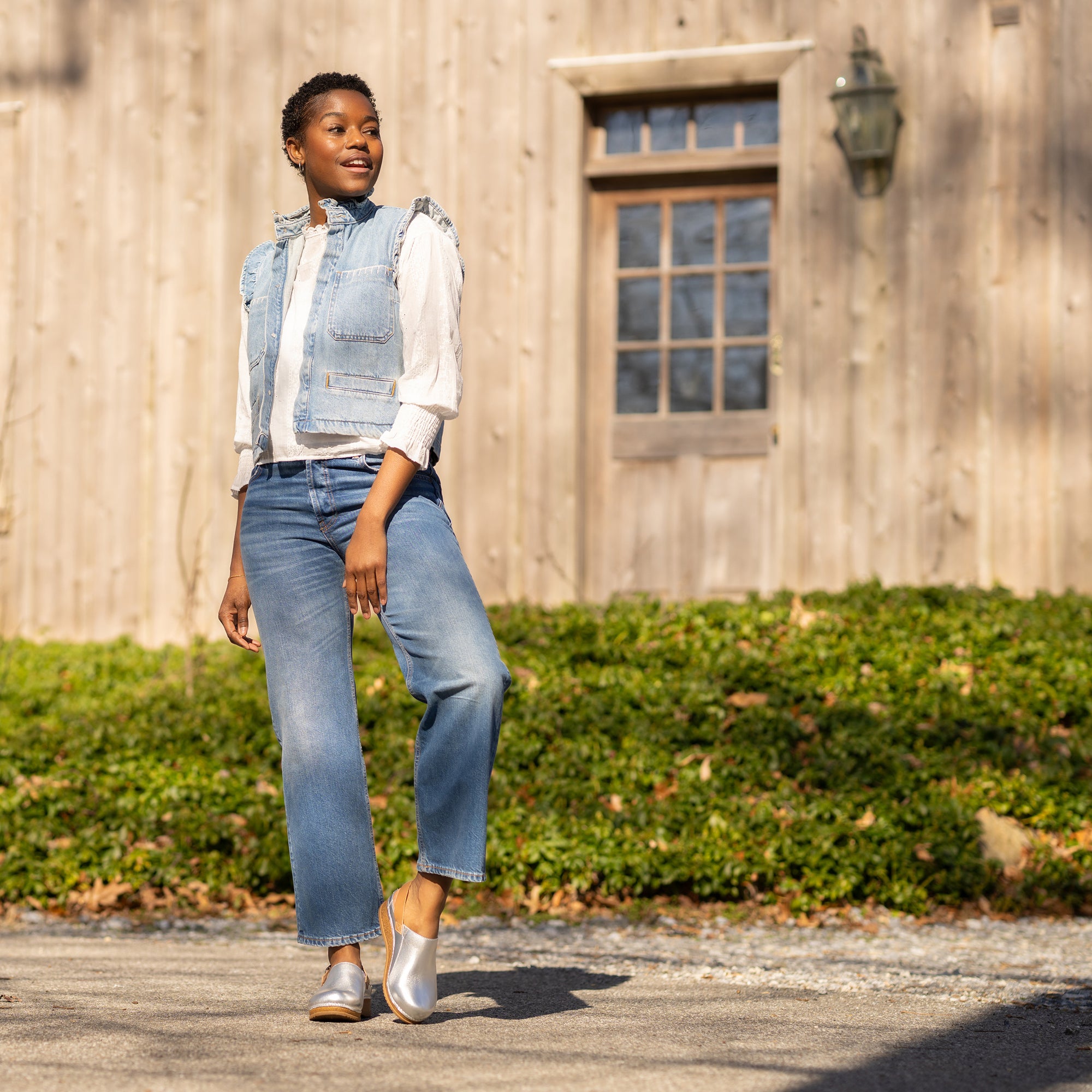 A woman in stylish denim attire wearing metallic leather mule clogs.