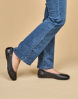 A closeup of black ballerina flats shown on foot.