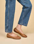 A closeup of brown ballerina flats shown on foot.