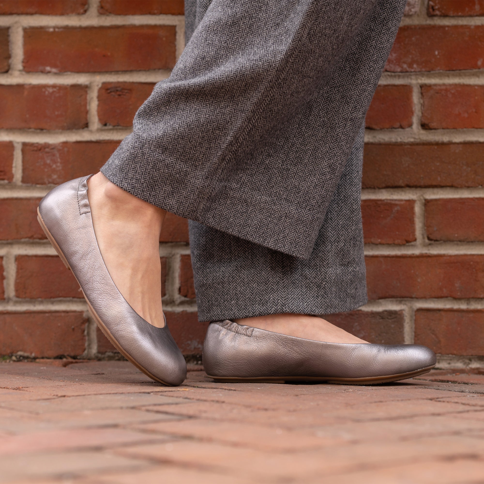 A closeup of metallic silver ballerina flats shown on foot.