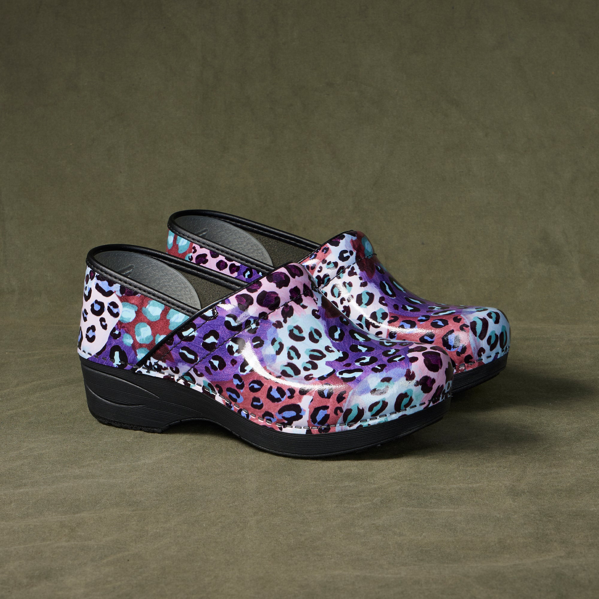 Leopard print patent clogs shown against a dark background.