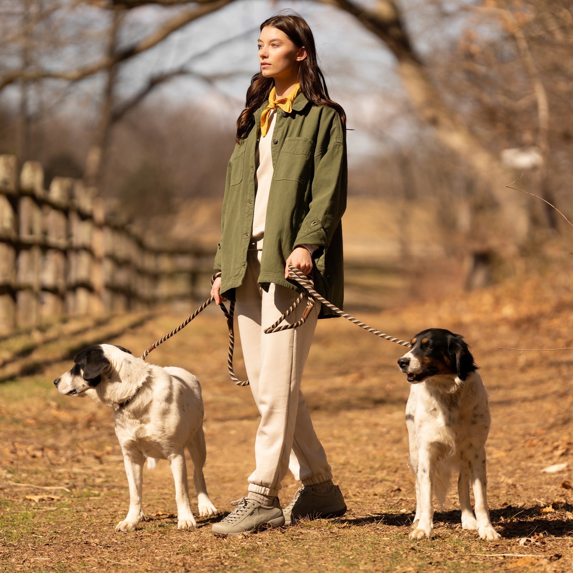 A woman with dogs on an outdoor trail wearing sage green trail sneakers.