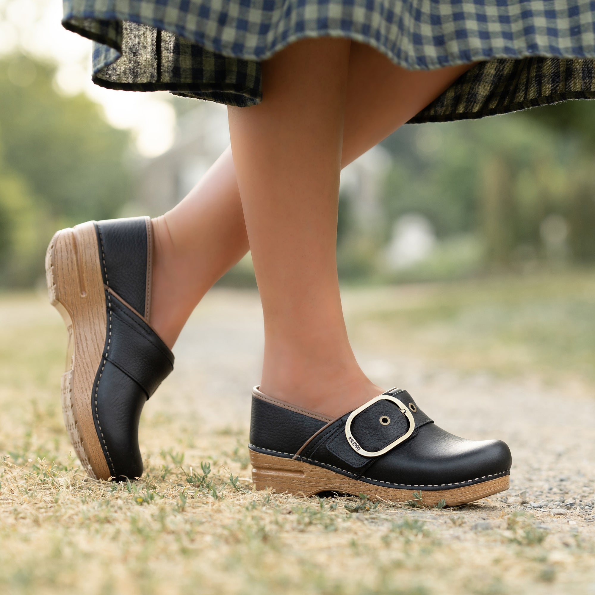 An on-foot shot of black clogs with a buckle that has &quot;Est. 1990&quot; detail.