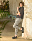 Woman standing against stone wall in dark shirt, grey jeans, and black platform Dansko clogs.
