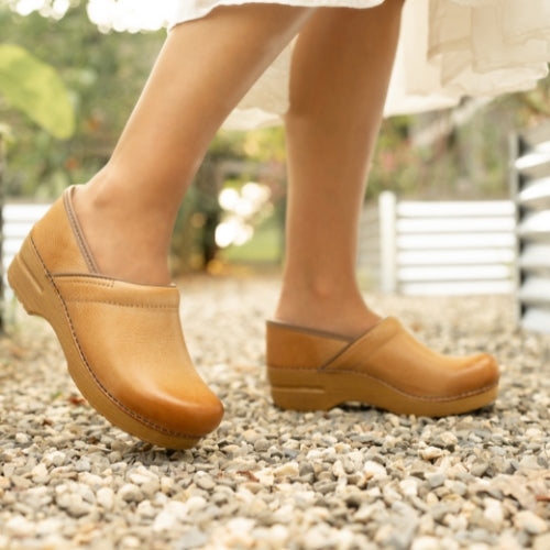 A close up of tan leather clogs stapled to a matching-color sole.