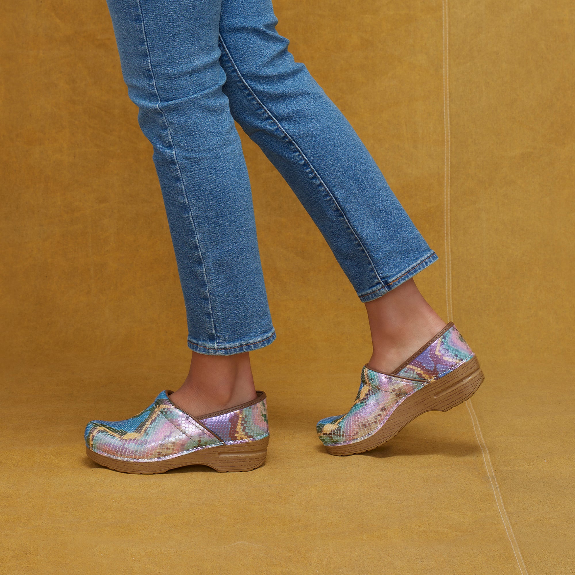 Colorful and shiny clogs on a faux wooden sole shown on foot.