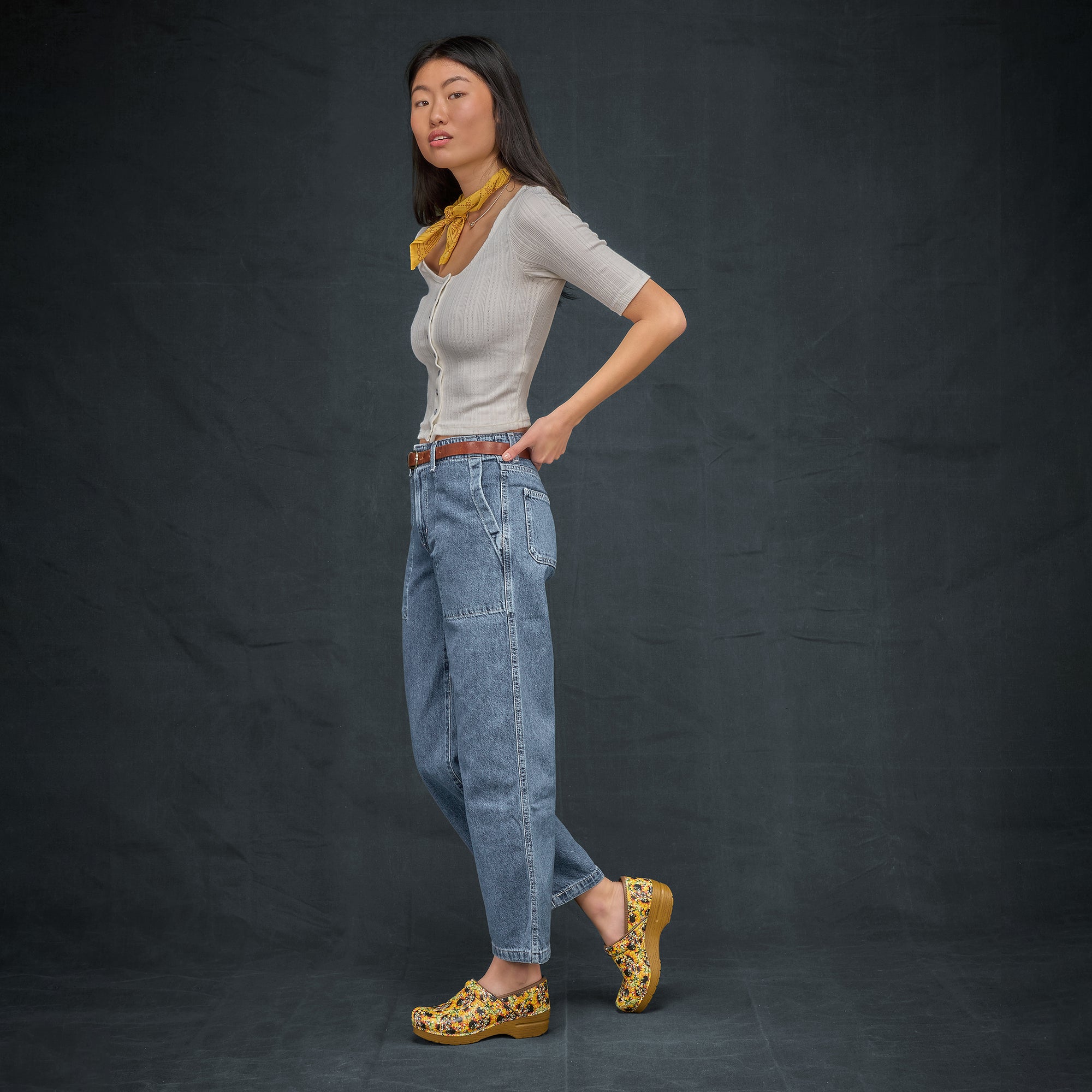 Woman in casual attire wearing bright, sunflower printed clogs.