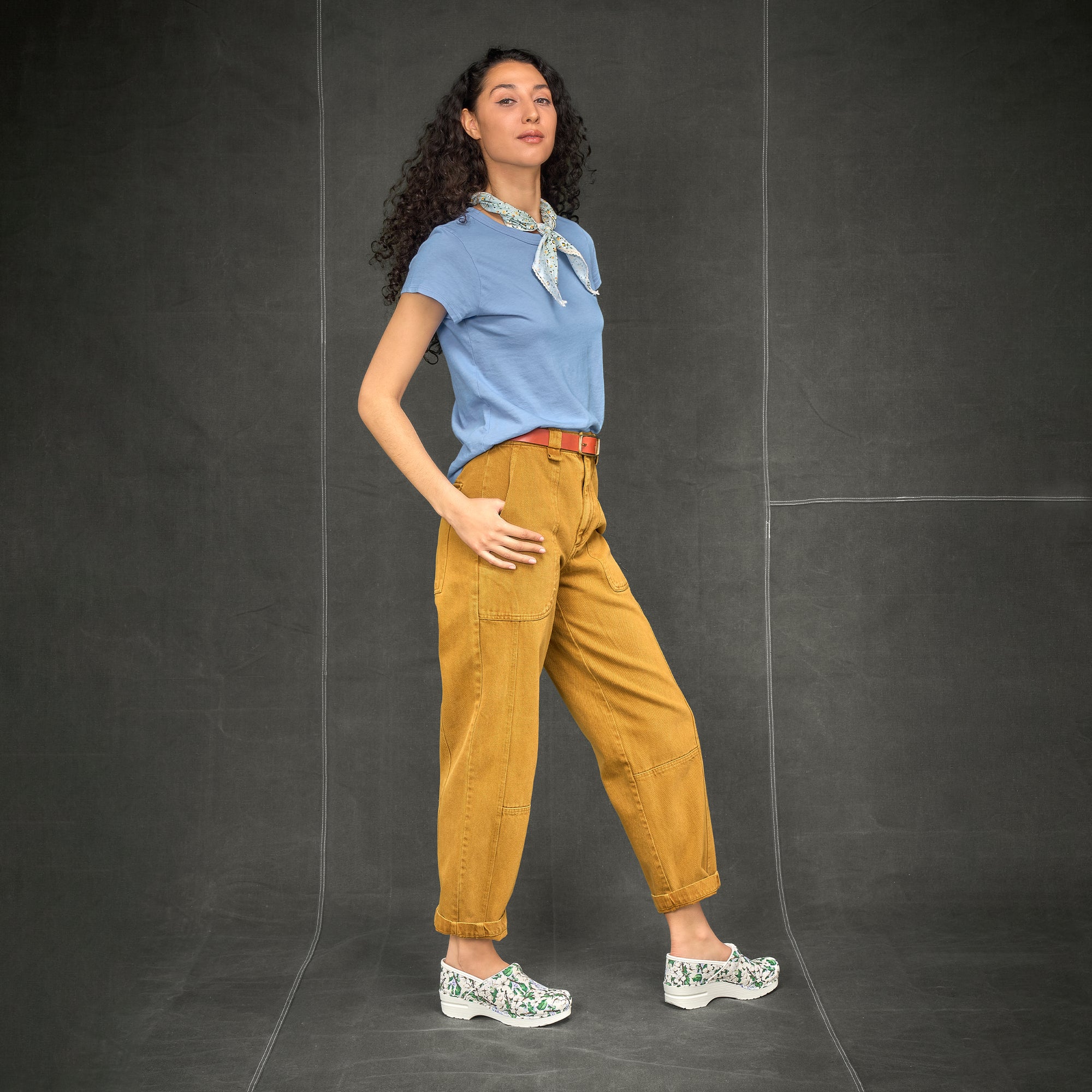 A woman standing confidently in a casual outfit while wearing white flower clogs.