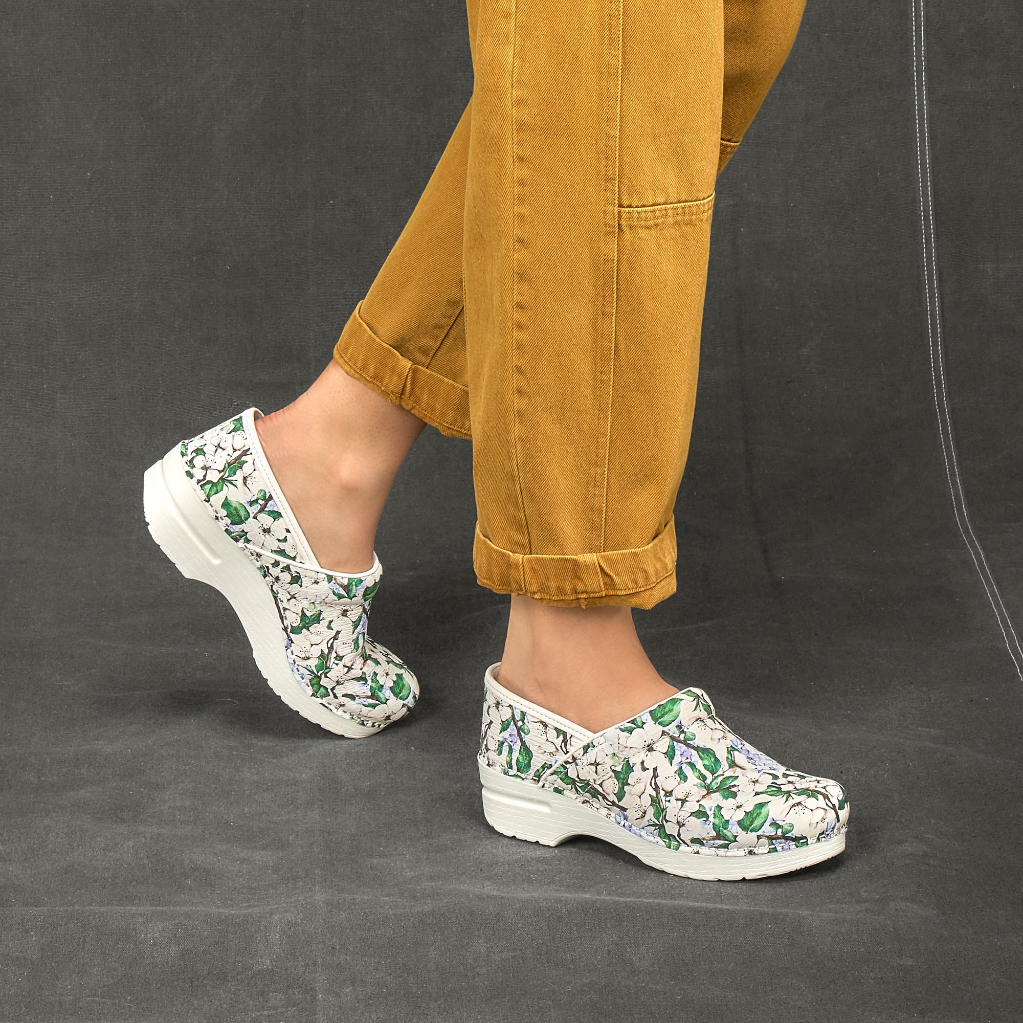 White-base clogs with a vine and flower pattern on leather uppers shown on foot.