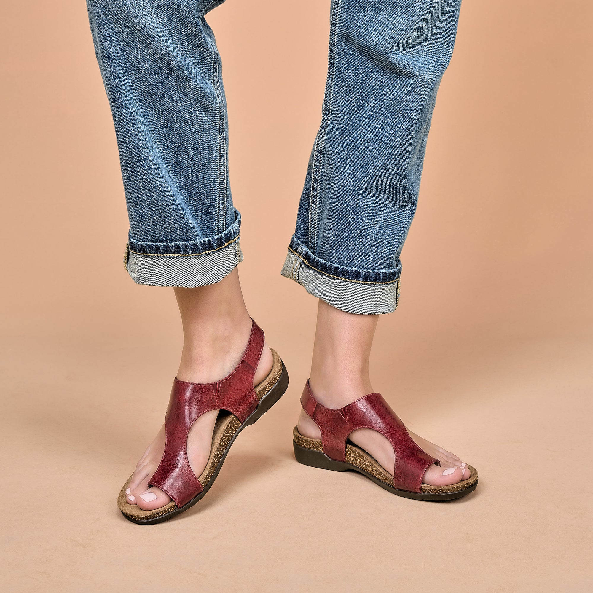 Red leather flat sandals with cork-based soles worn with jeans.