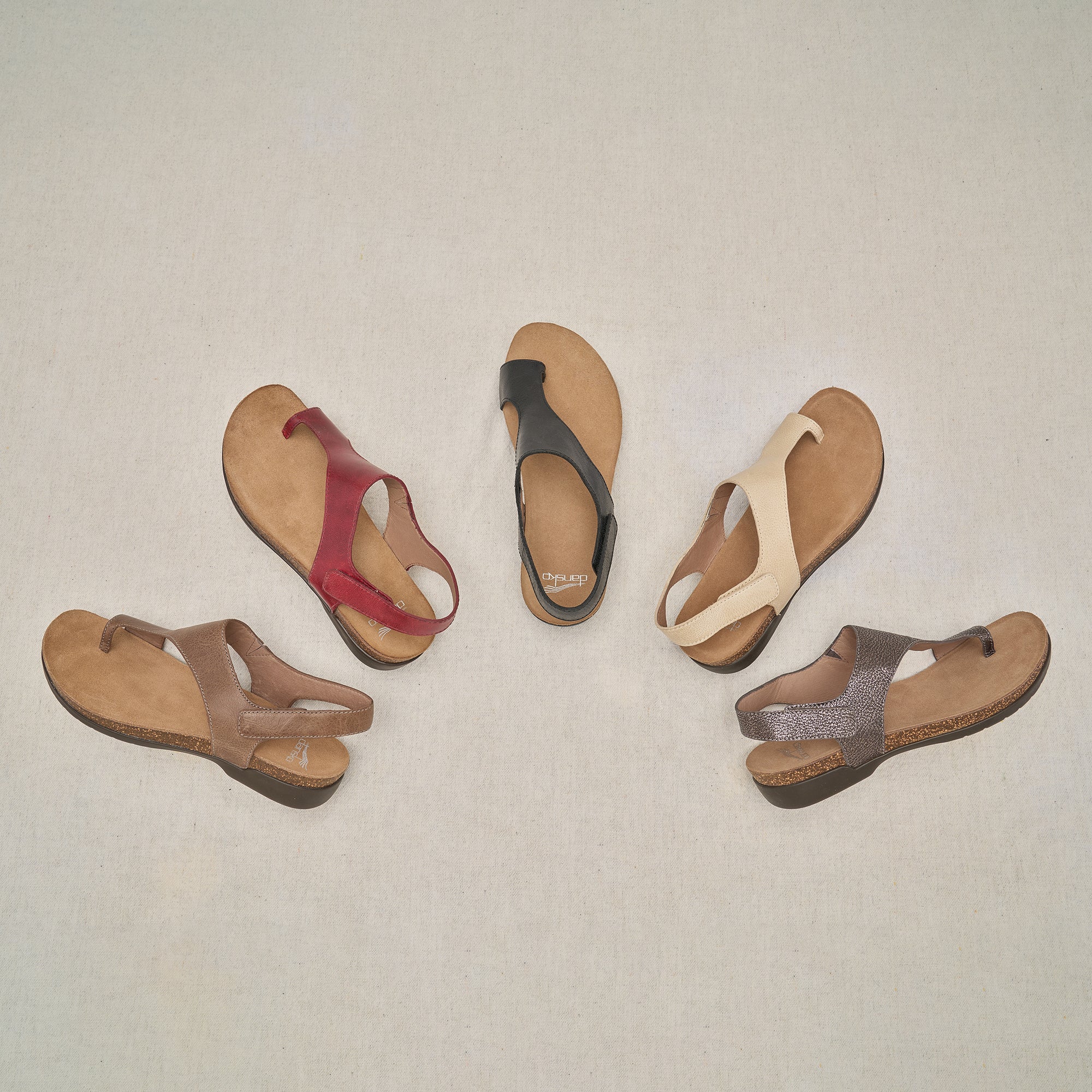 Five different colors of a flat, leather toe-post sandal.