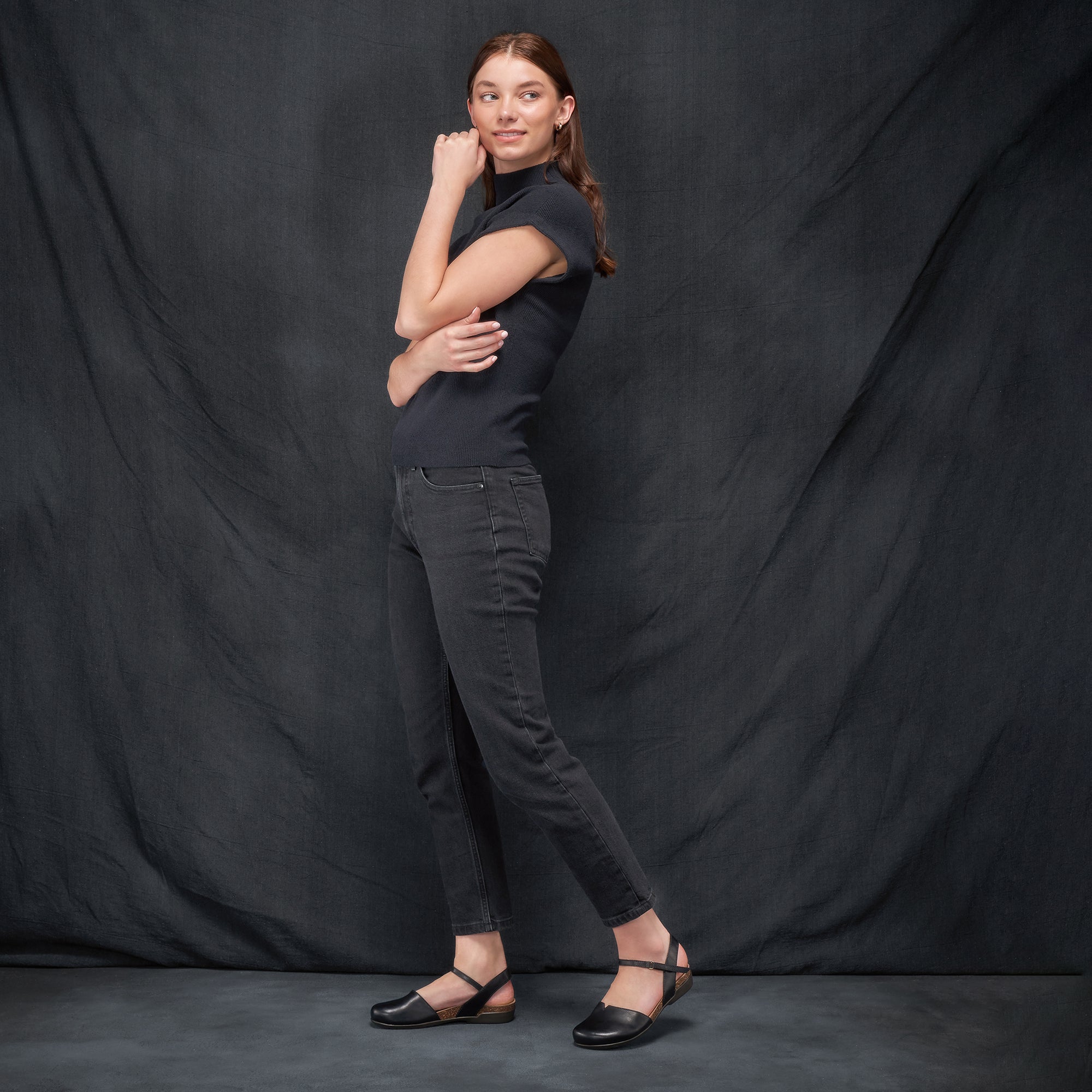 A woman in a dark casual outfit in black waxy transitional sandals.