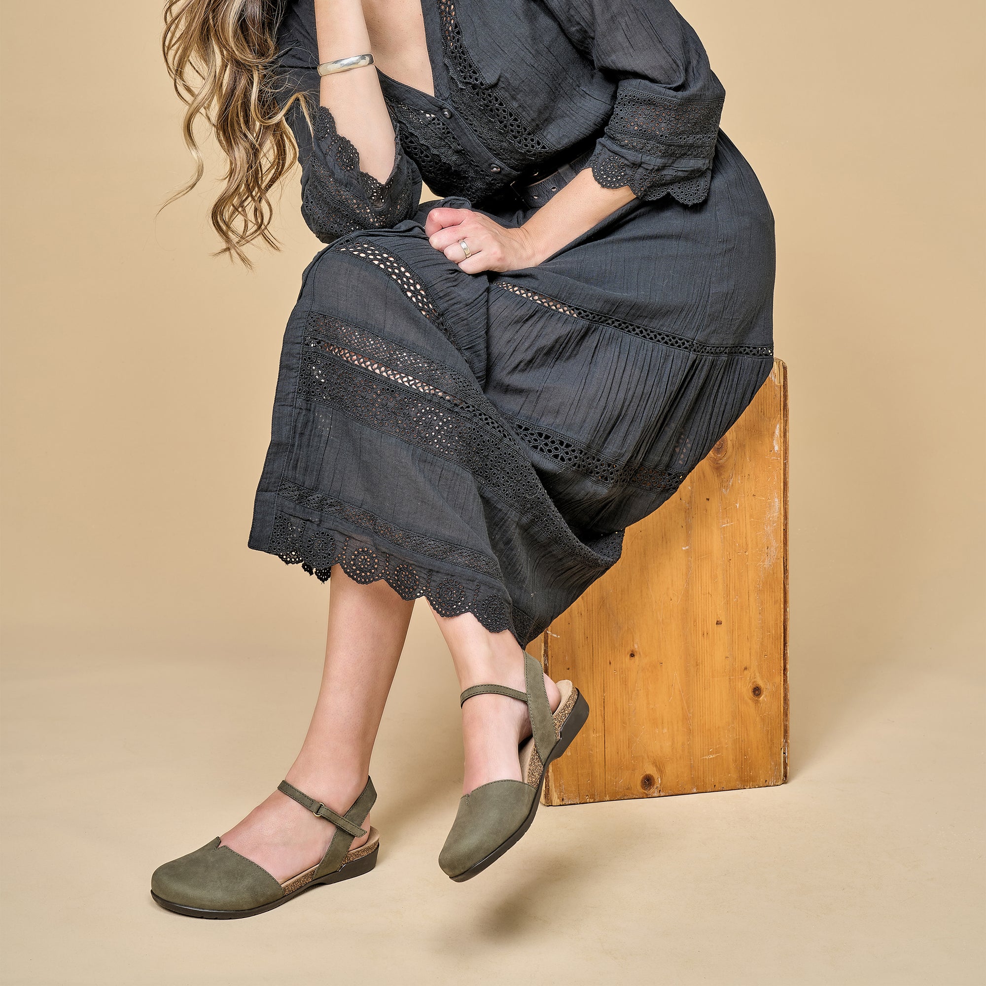 A woman in a flowy dress wearing neutral green transitional sandals.