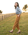 A woman standing in a field wearing brown waxy leather closed-toe sandals.