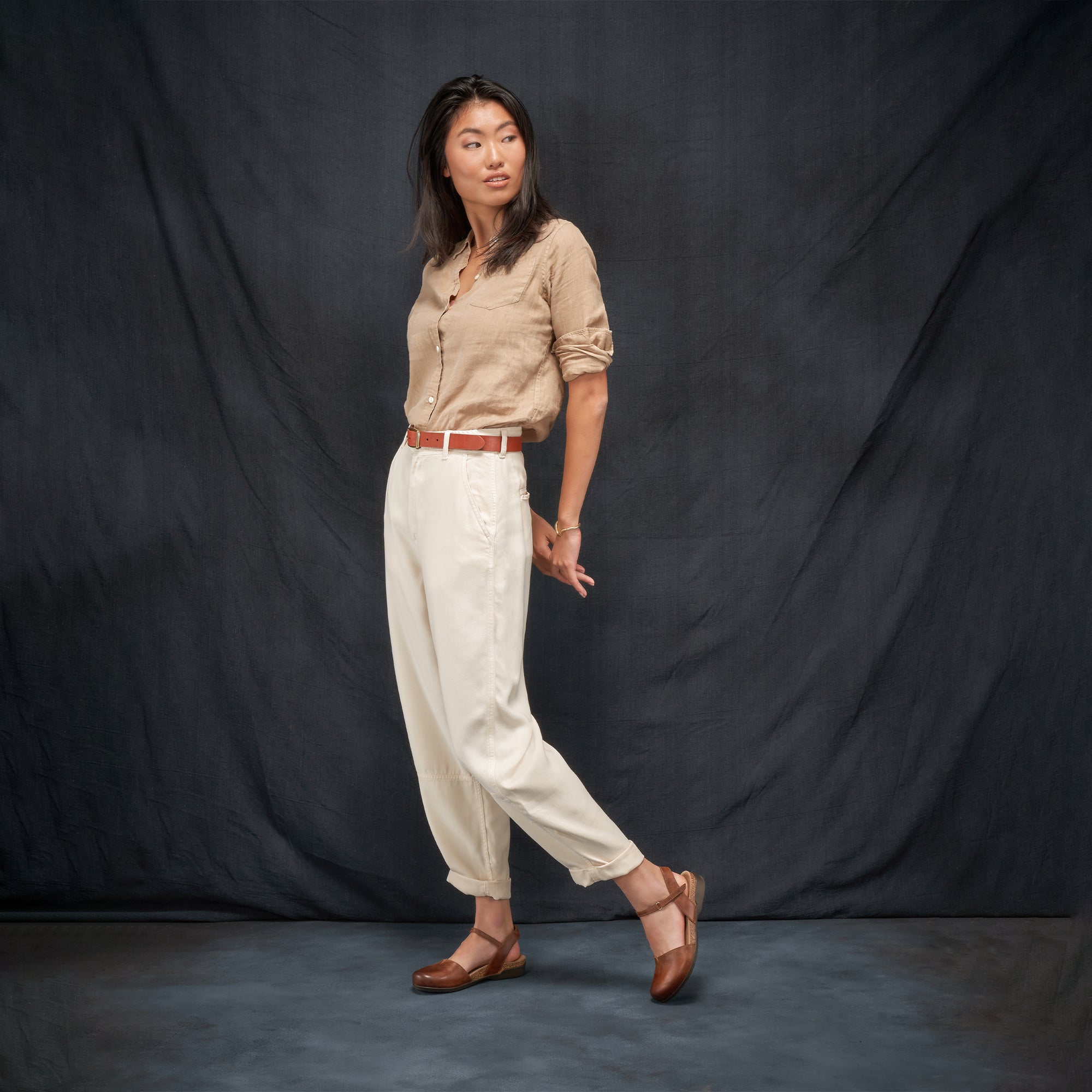 A woman in a monochromatic earth tone outfit wearing brown leather transitional sandals.