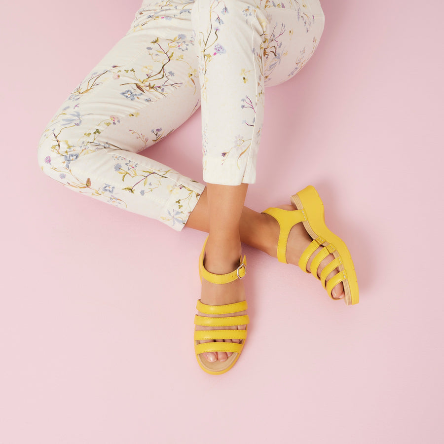 A woman wearing flowery pants and bright yellow sandals.