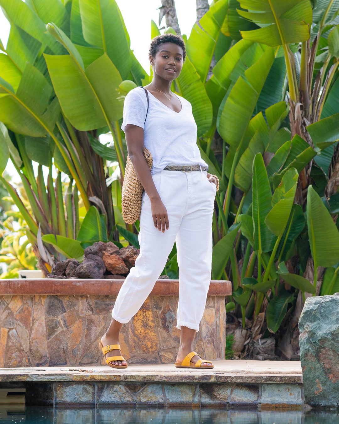 A woman in all white standing next to a pool while wearing yellow flat slide sandals.