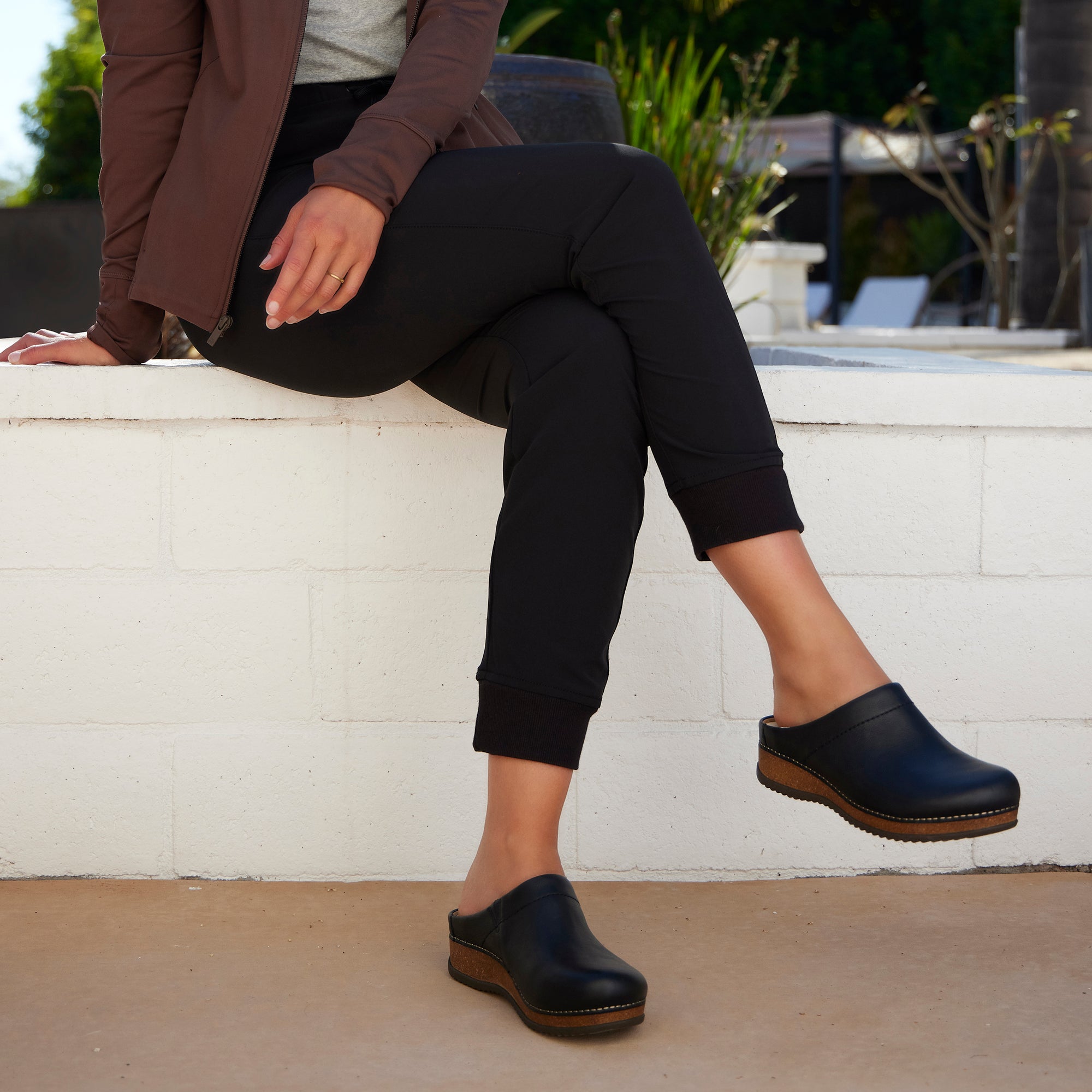Woman in a stylish outfit wearing black mule clogs with cork-based sole.