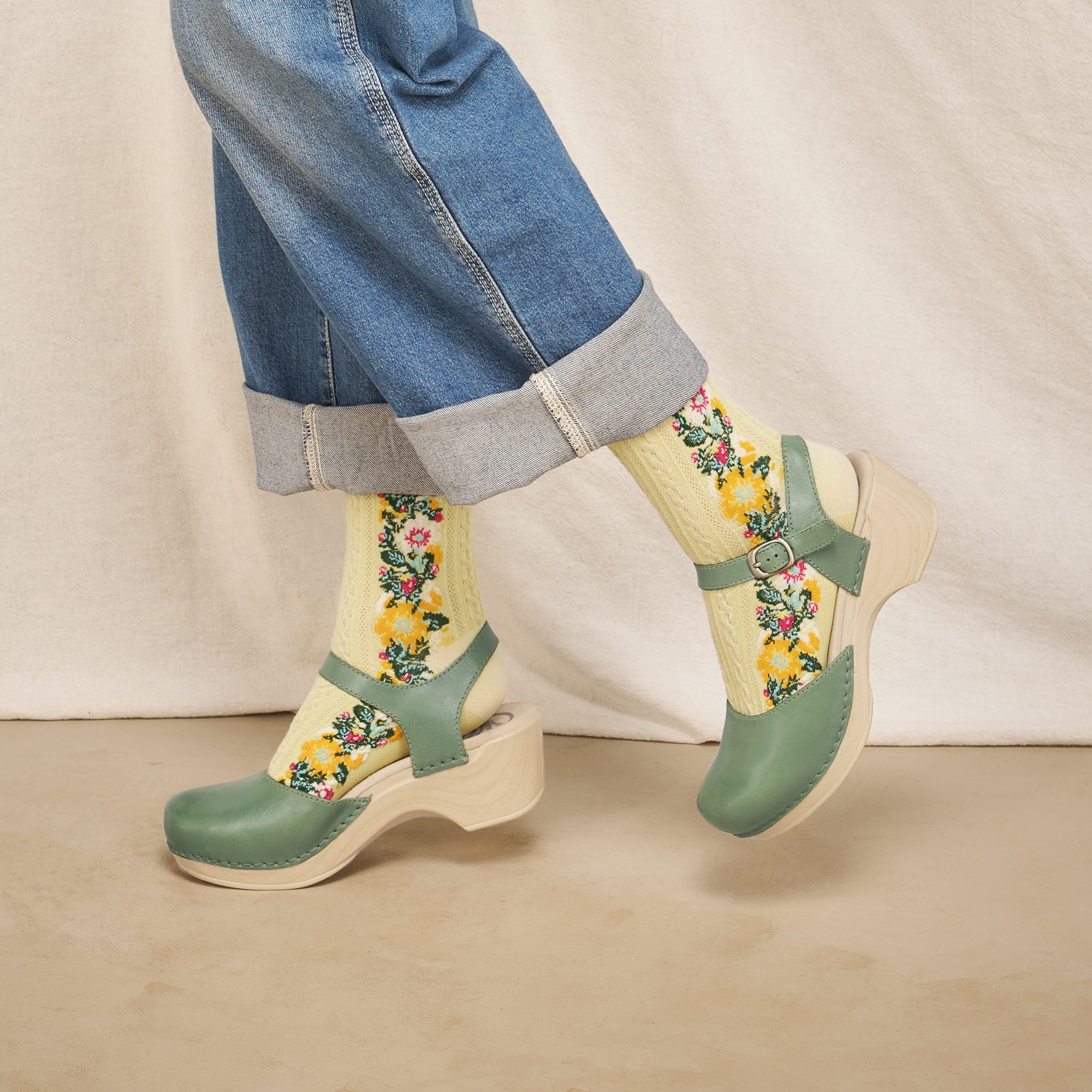 A close up look of green sandals worn with floral socks and shown on foot.