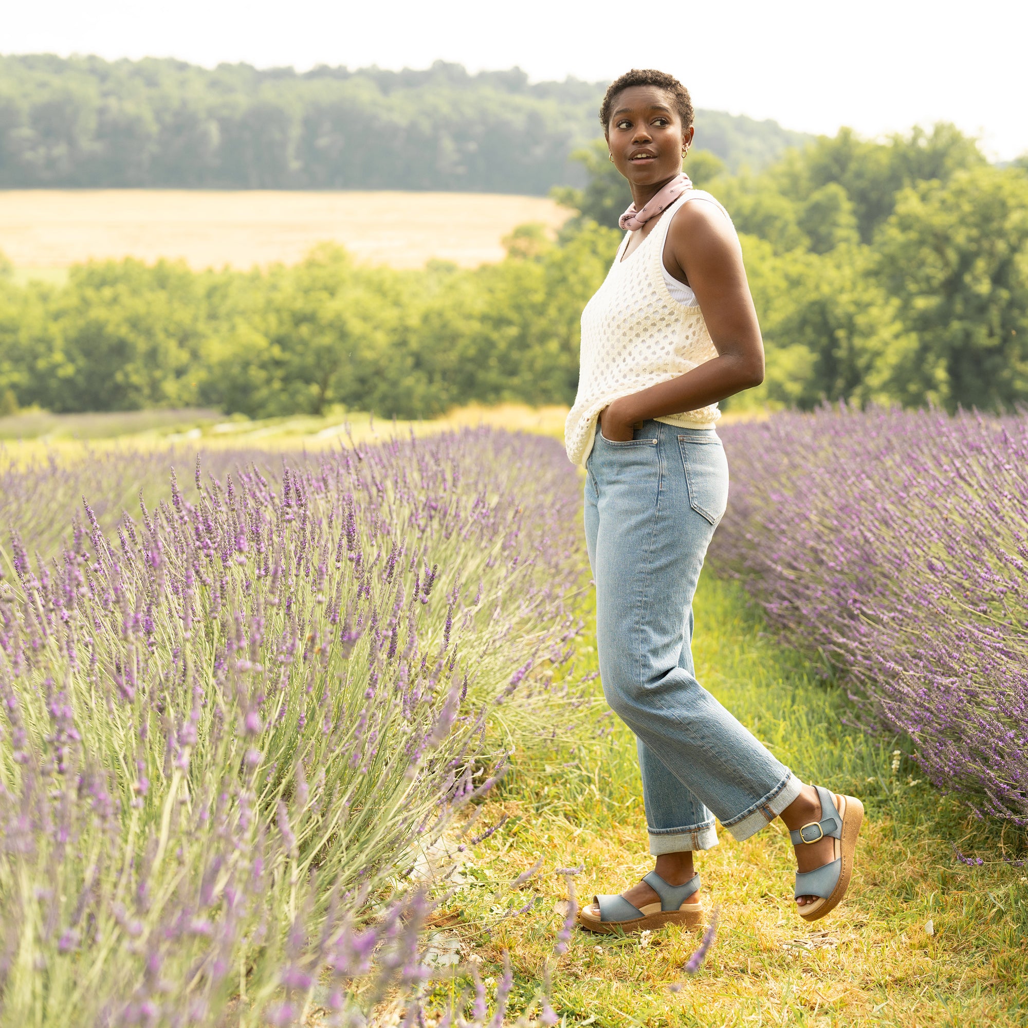 Woman in lavender field wearing a crochet tank top, jeans, and blue Dansko sandals.