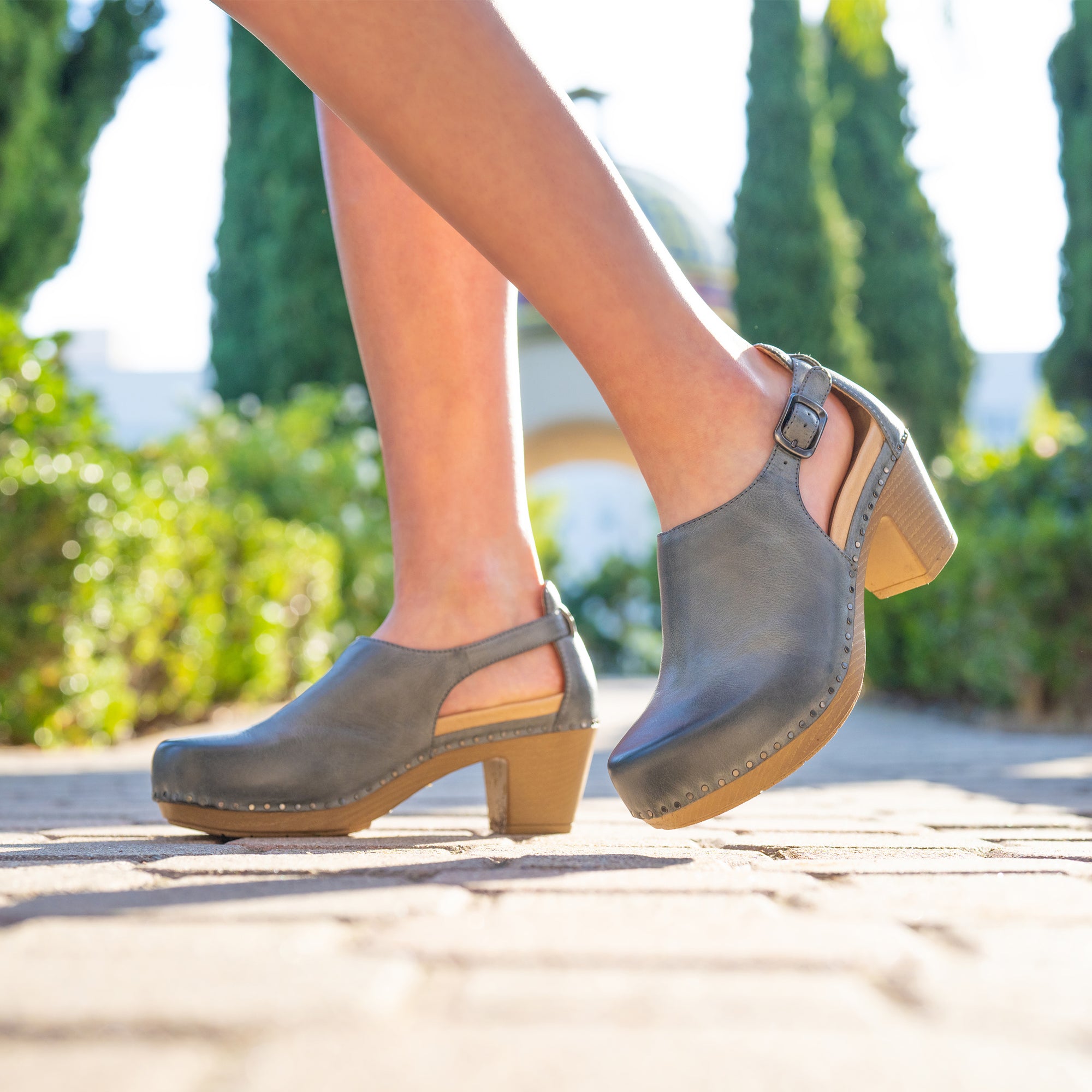 A closeup of light grey leather heels made with stylish nail-head construction shown on foot.