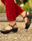 A black sandal with a clog sole styled with seasonal red jeans.