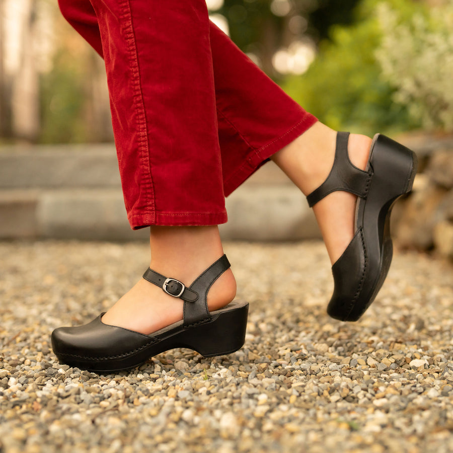 A black sandal with a clog sole styled with seasonal red jeans.