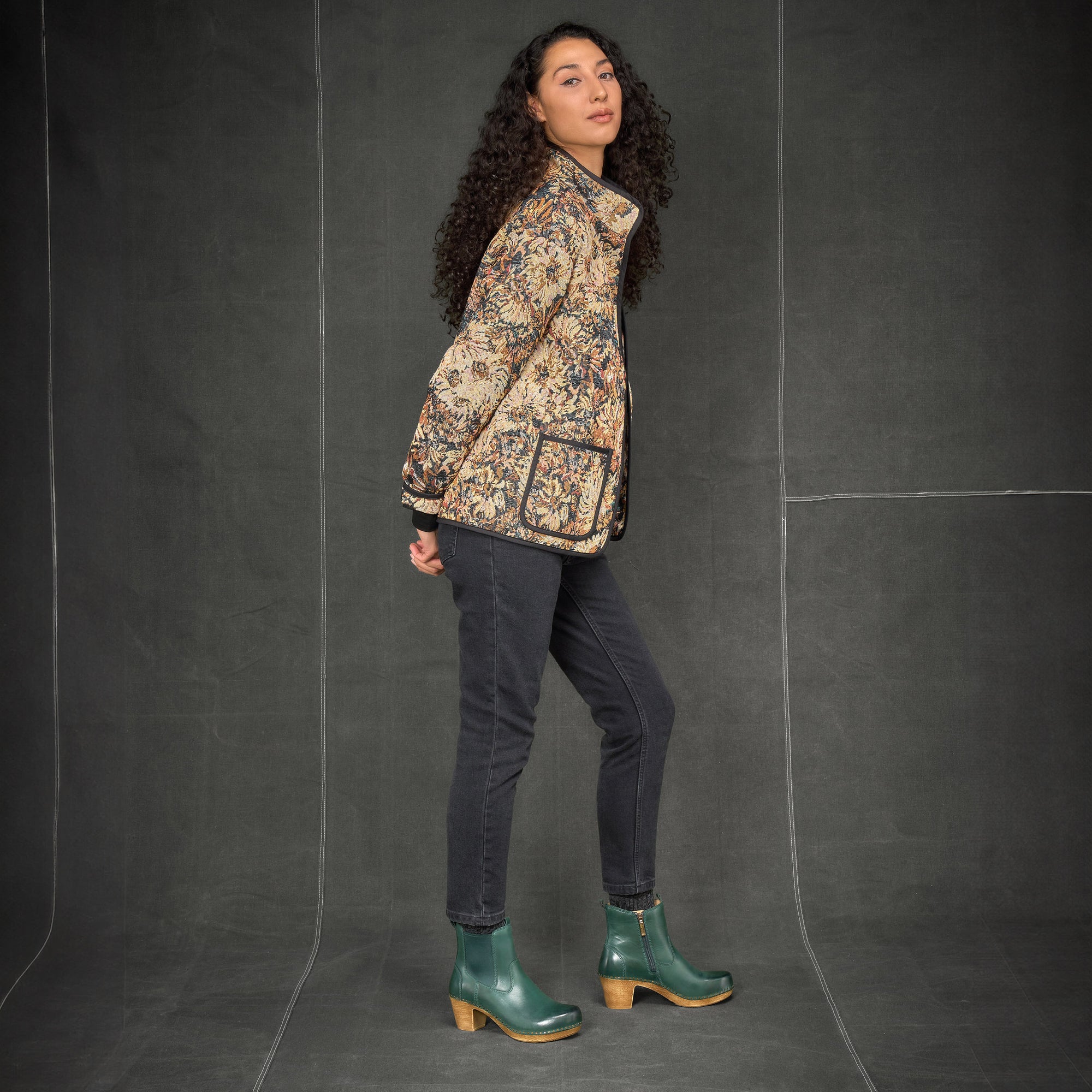 A woman wearing green heeled boots with black jeans and a floral coat.